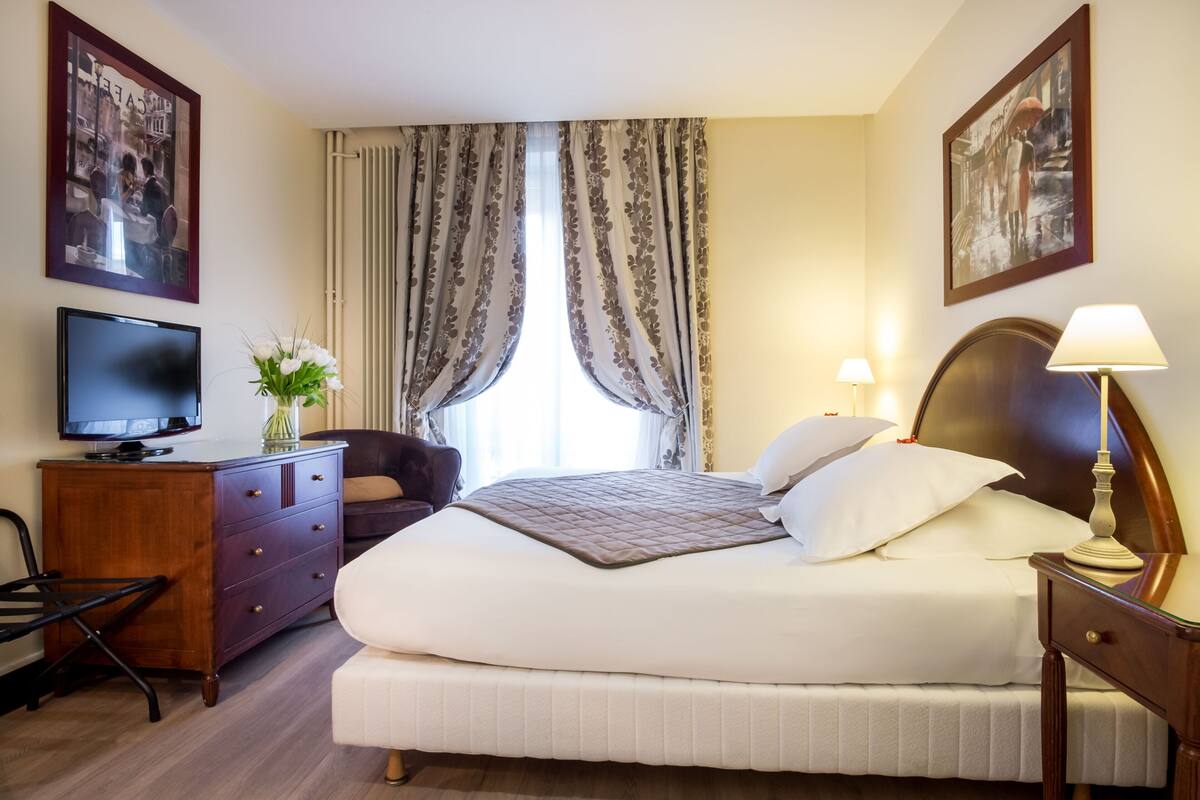 Une chambre d’hôtel avec un lit, un bureau, une chaise, une télévision et des rideaux.