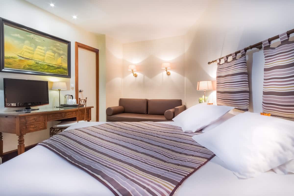 Une chambre d’hôtel comprenant un lit, un bureau avec une télévision, un canapé et deux lampes fixées au mur.