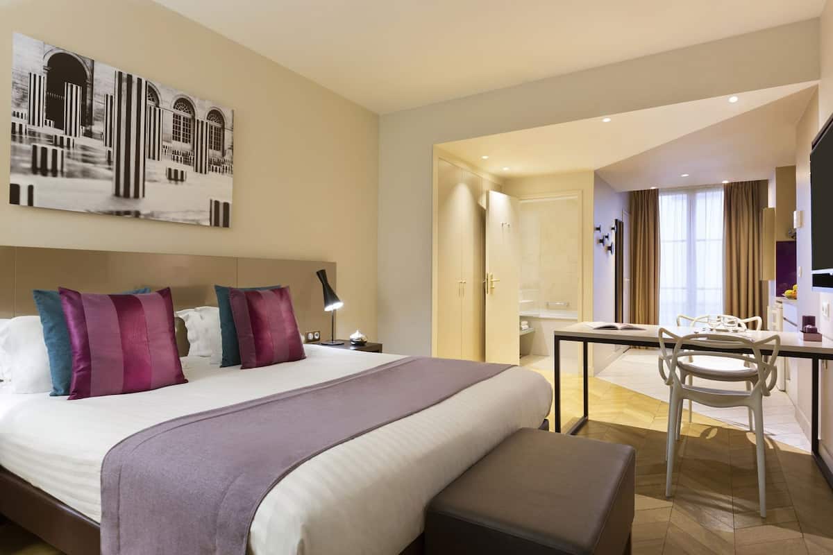 Ein Hotelzimmer mit einem großen Bett, Nachttischen, einem Schreibtisch mit Stühlen, einem Badezimmer und einem Fernseher.