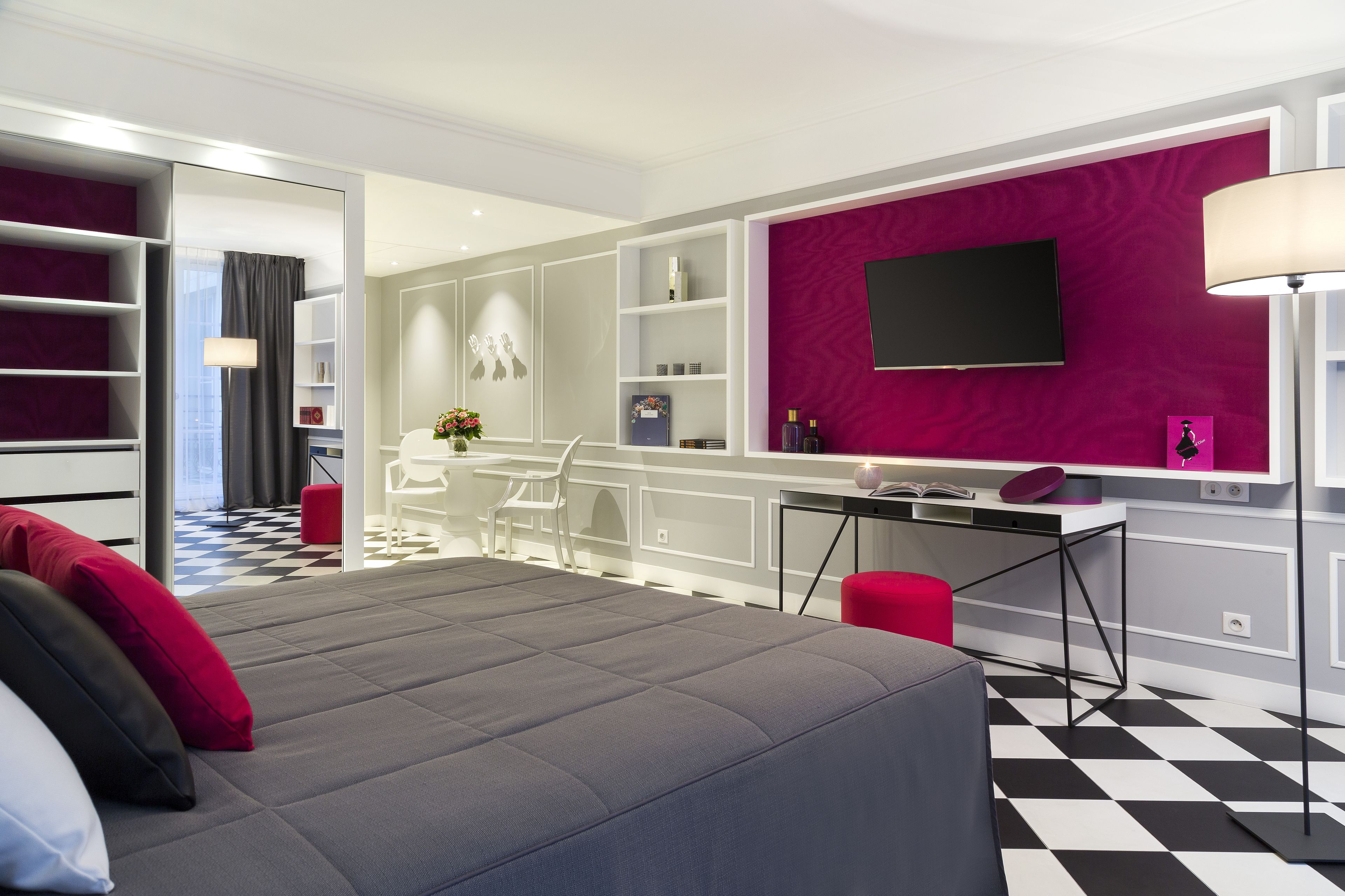 A modern hotel room with a large bed, a desk, a TV, and a vibrant purple accent wall.