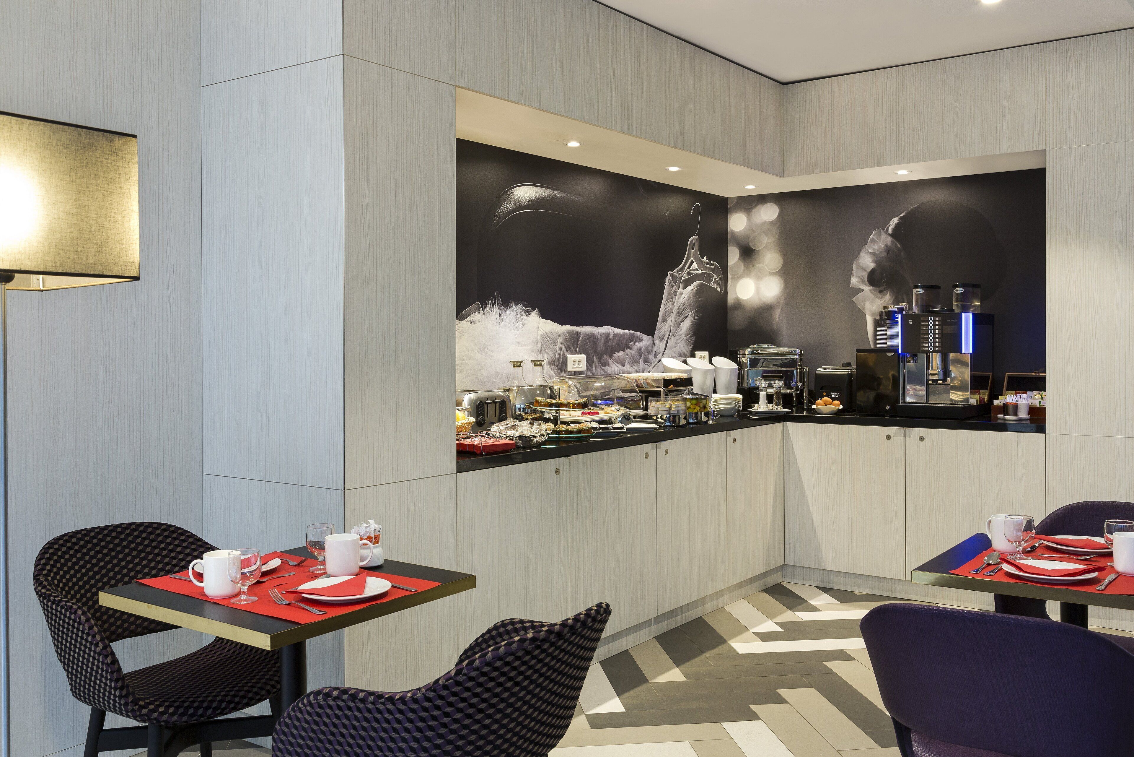 A modern hotel room with a dining area, a large wall mural, and a kitchenette.