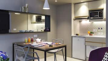 Eine moderne Küche mit Essbereich, ausgestattet mit einer Mikrowelle, einem Kühlschrank und einem Esstisch, der mit Tellern, Gläsern und einem Blumenstrauß gedeckt ist.