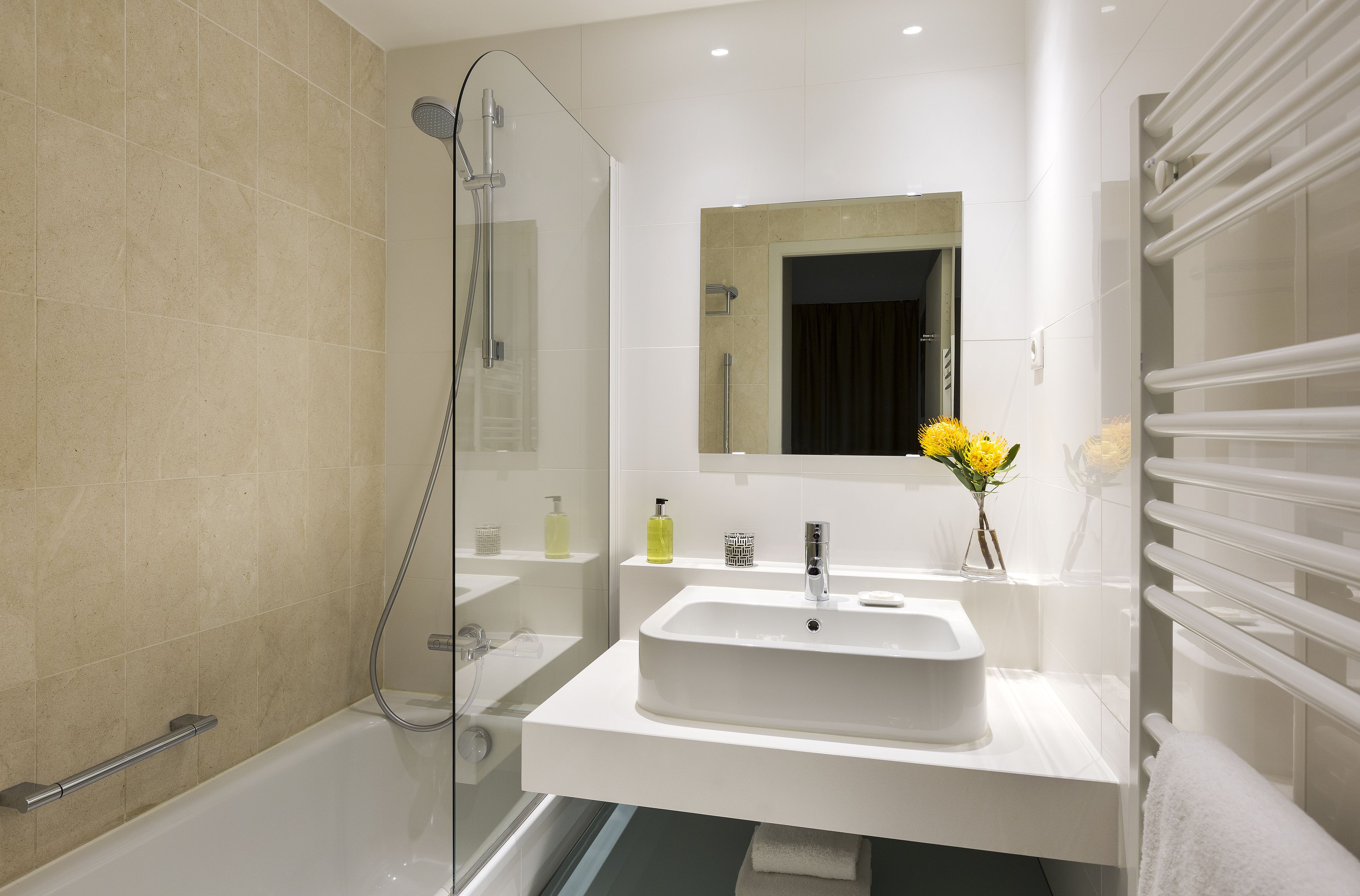 Un baño moderno con bañera, ducha con mampara de vidrio, lavabo blanco con espejo y un toallero.