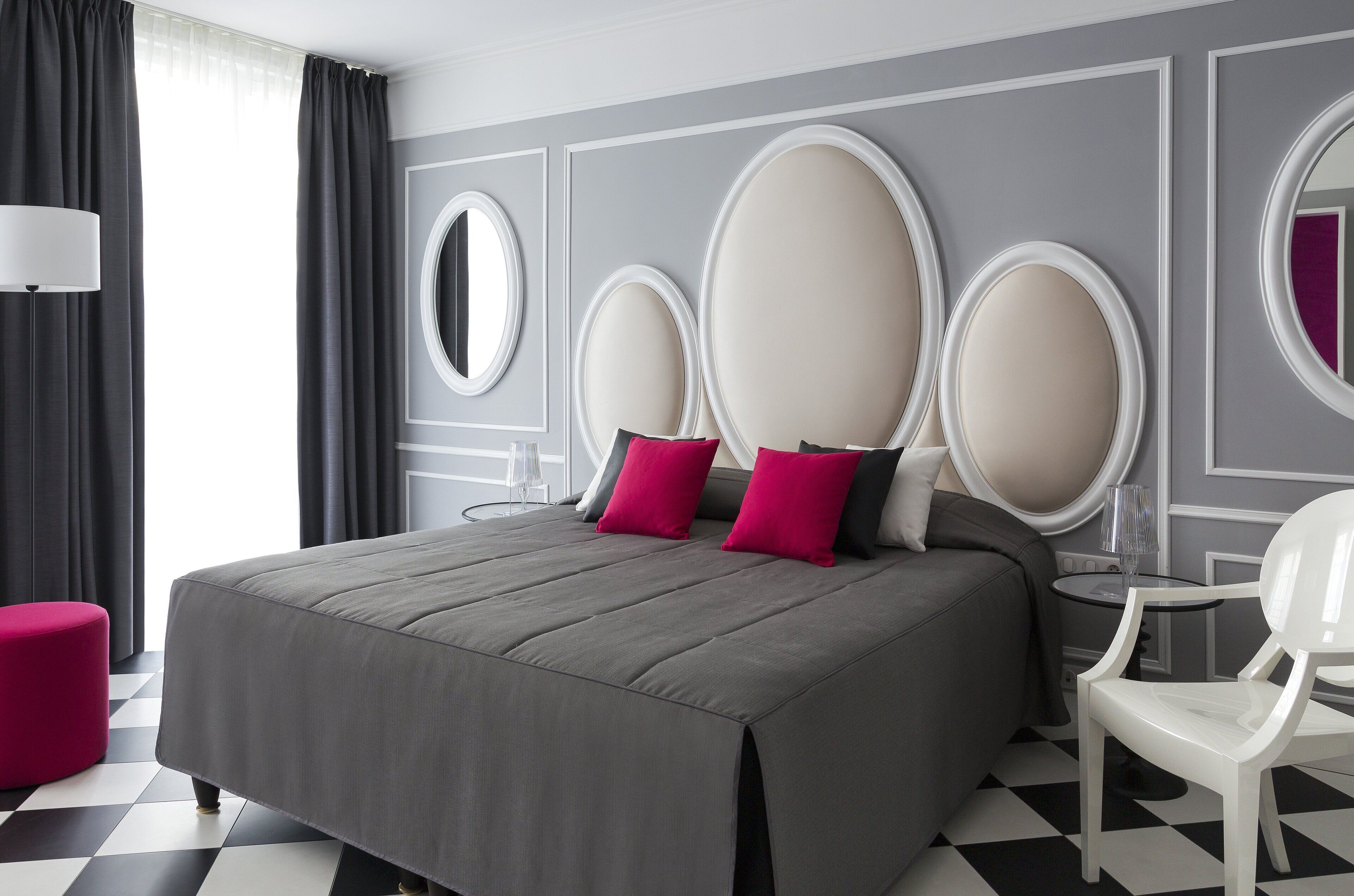 Une chambre d’hôtel avec un grand lit, deux miroirs ronds, une petite table, une chaise et une lampe.
