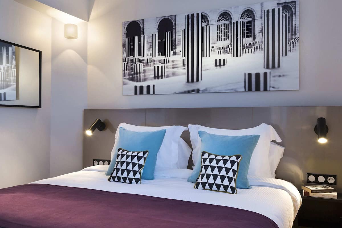 Ein Hotelzimmer mit einem Bett, zwei Kissen, einem Nachttisch, einer Wandlampe und einem gerahmten Bild über dem Bett.