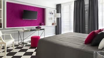 Ein modernes Hotelzimmer mit einem großen Bett, einem Schreibtisch, einem Sessel und einem Fernseher an einer leuchtend pinken Wand.