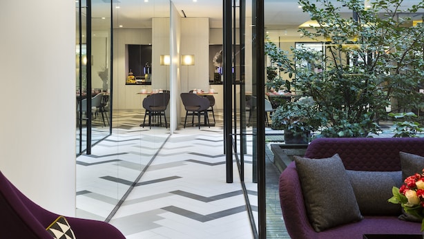 Een moderne lobby met een glazen scheidingswand, een paarse bank en een eethoek met stoelen en tafels.