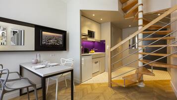 A modern kitchen with a herringbone floor pattern, a dining area with a white table and chairs, and a wooden spiral staircase.