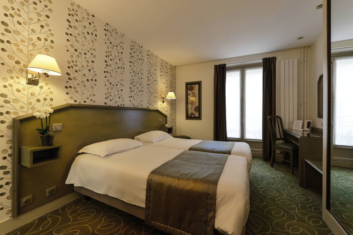 A hotel room with two beds, a desk, a chair, a lamp, and a window with curtains.