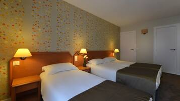 Habitación de hotel con dos camas, una mesita de noche con lámpara y una pared con estampado floral.