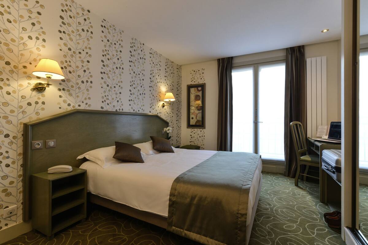 A hotel room with a large bed, bedside lamps, a desk, and a chair.