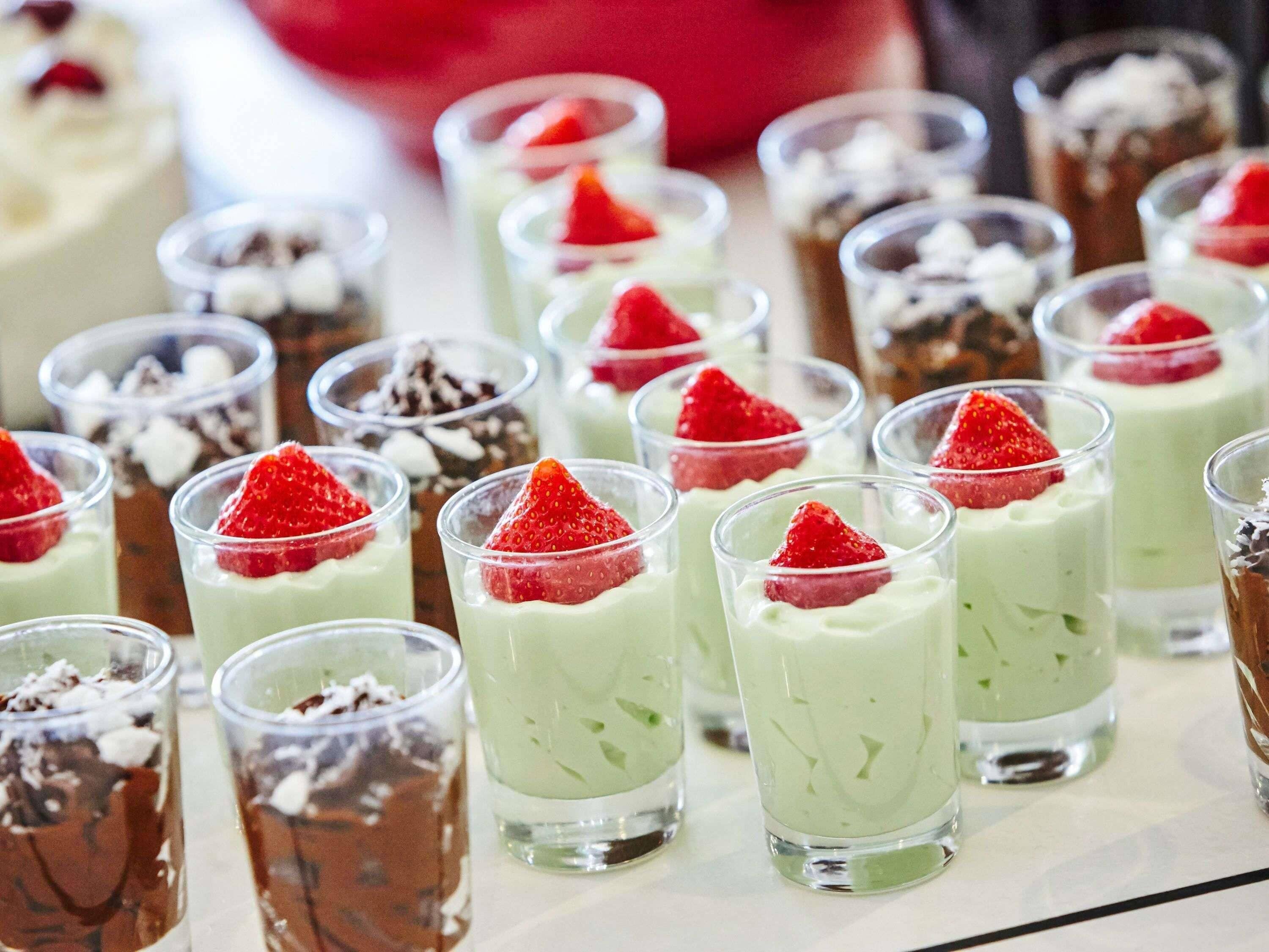 A variety of desserts in clear glasses, some topped with strawberries.