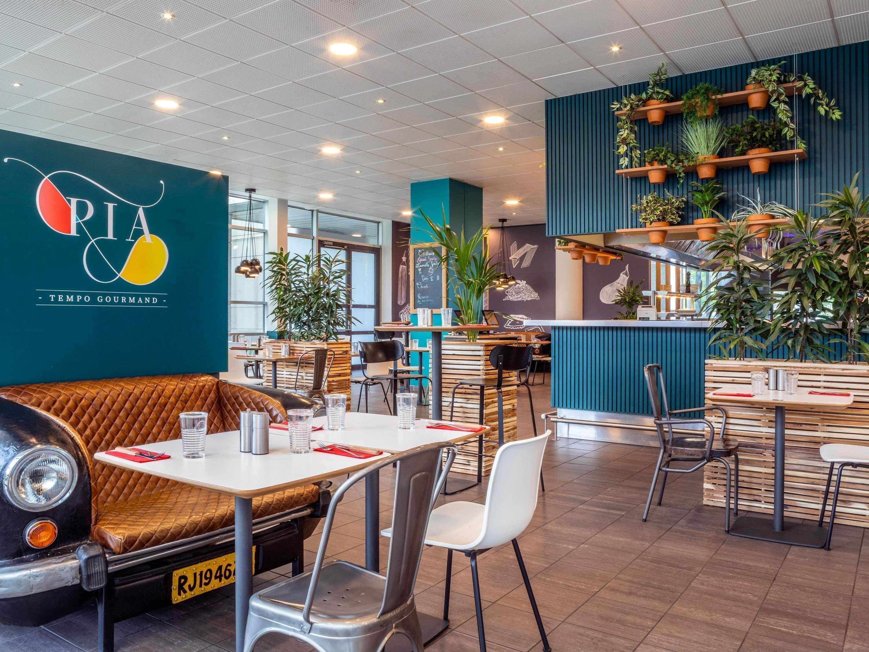 Ein Restaurantinneres mit einer Sitzgruppe in Form eines Oldtimers, Tischen, Stühlen und einer Wand mit Logo und Speisekarte.
