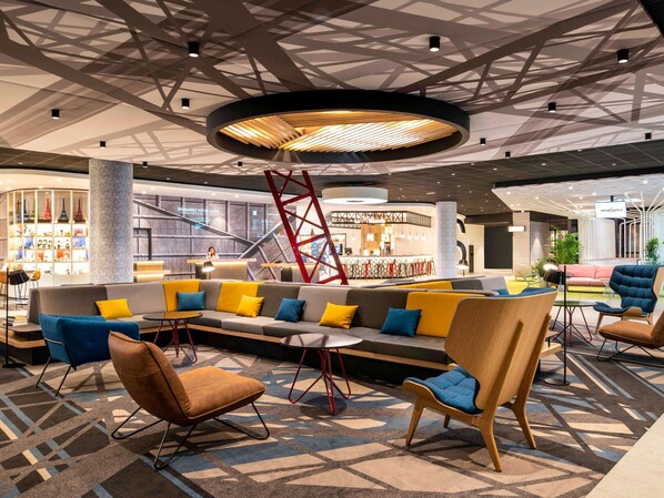 Relax in the hotel lobby's central seating area, featuring a sofa and armchairs, alongside a reception desk and bar.