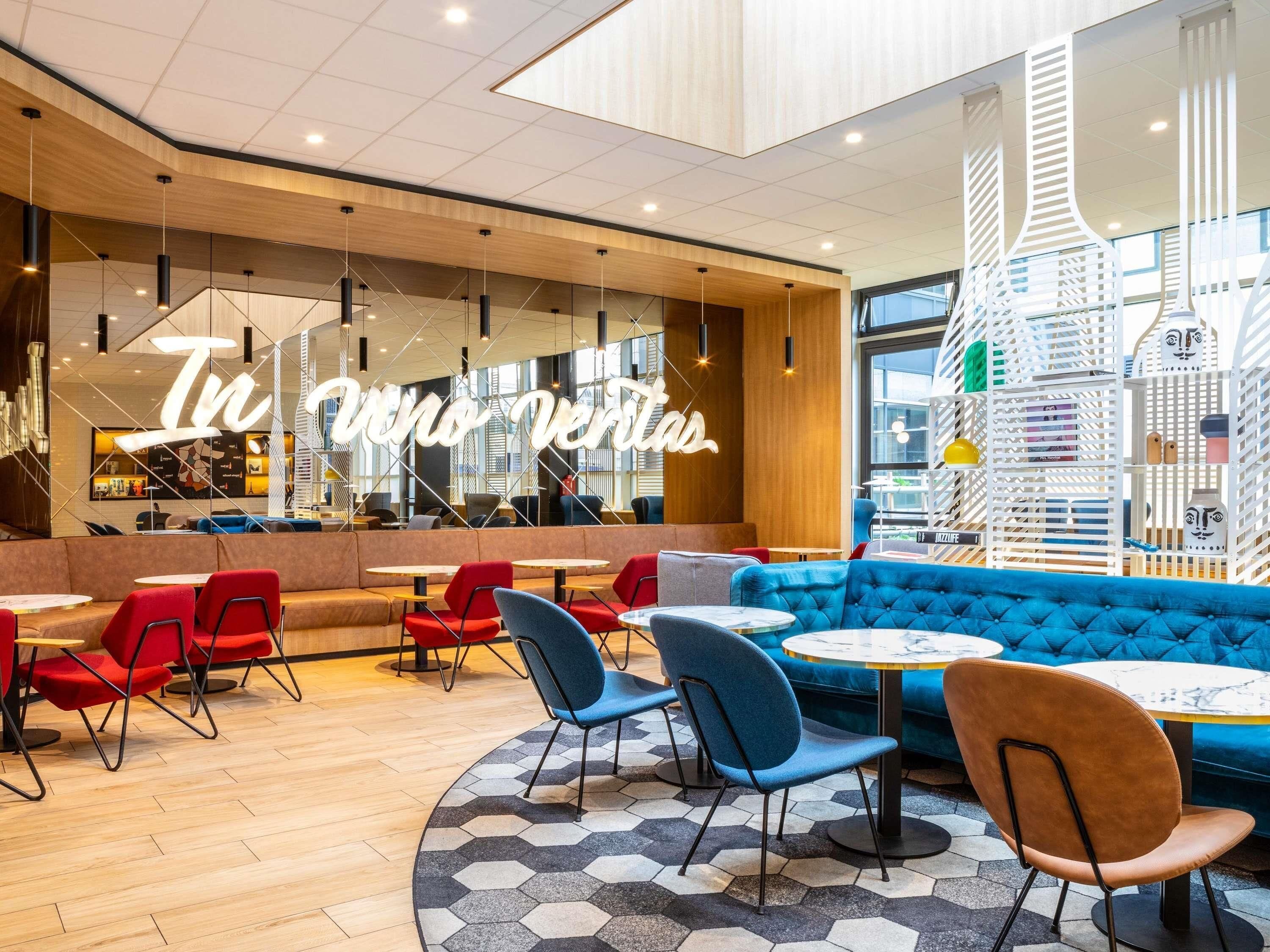 A modern cafe with a large illuminated sign, comfortable seating, and a view of the cityscape through large windows.