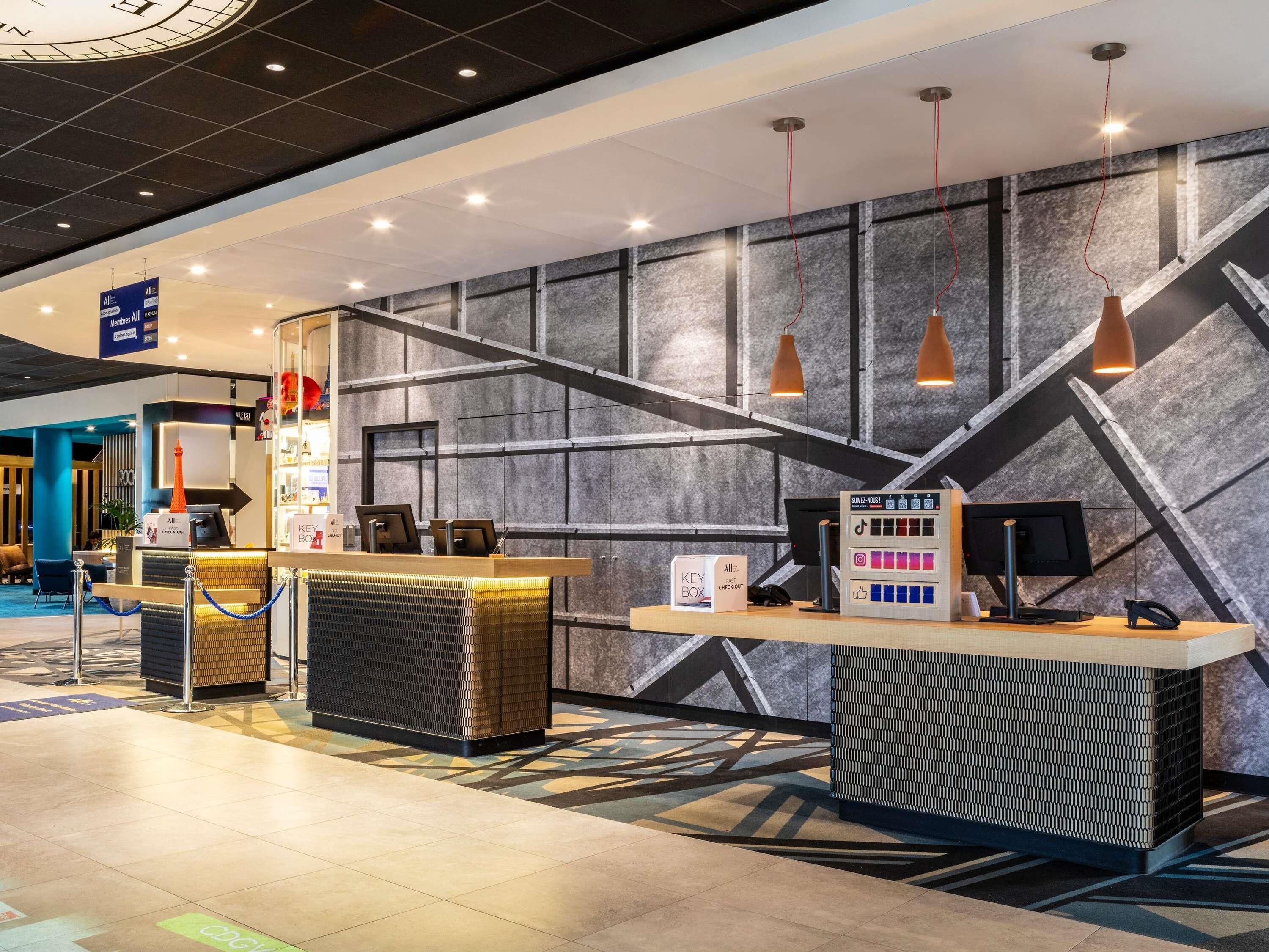 Zona de recepción de hotel con diseño moderno, que incluye un mostrador de recepción, un buzón para llaves y una pantalla digital para el registro.