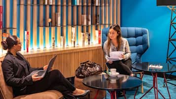 A modern lounge area with a blue wall, a bookshelf, and two seating areas with tables.