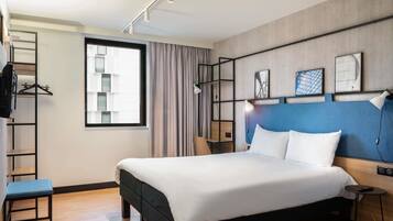 A modern hotel room with a large bed, a desk, a chair, a wardrobe, and a window with curtains.