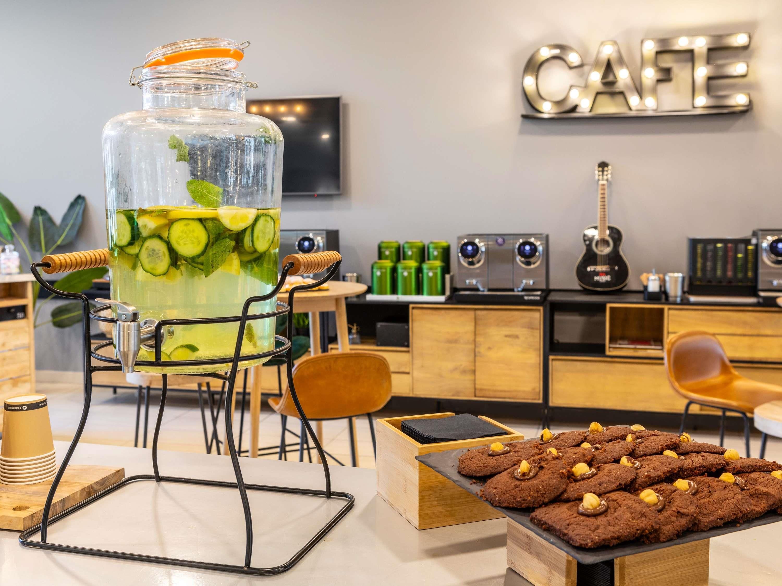 A modern cafe interior with a large glass beverage dispenser, a guitar, and a display of cookies.