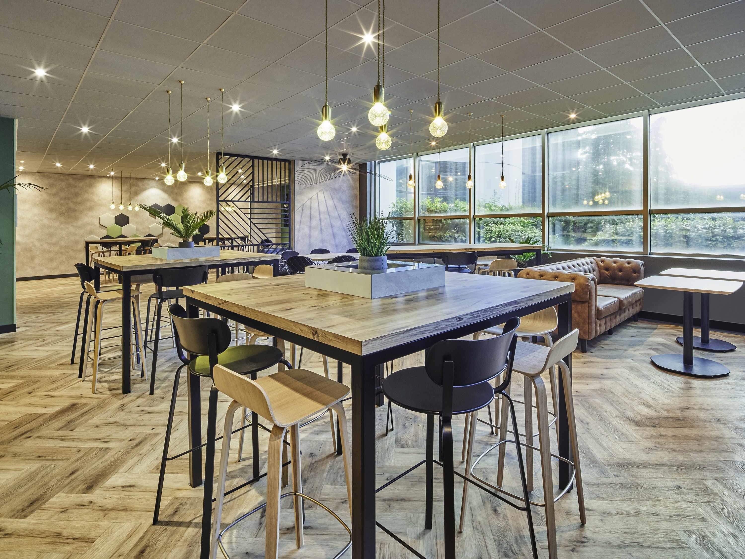 Un espace de restauration moderne avec des tables et des chaises en bois, de grandes fenêtres et des luminaires suspendus.