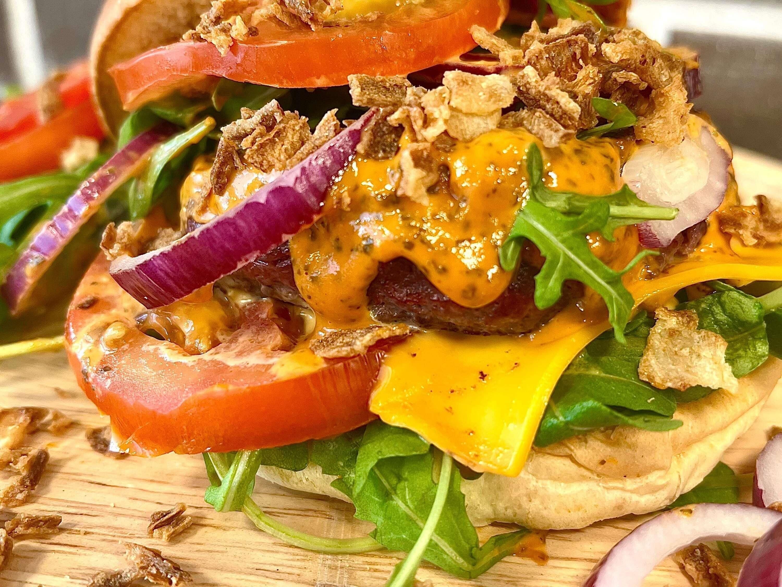 A sandwich with various toppings and a side salad on a wooden board.
