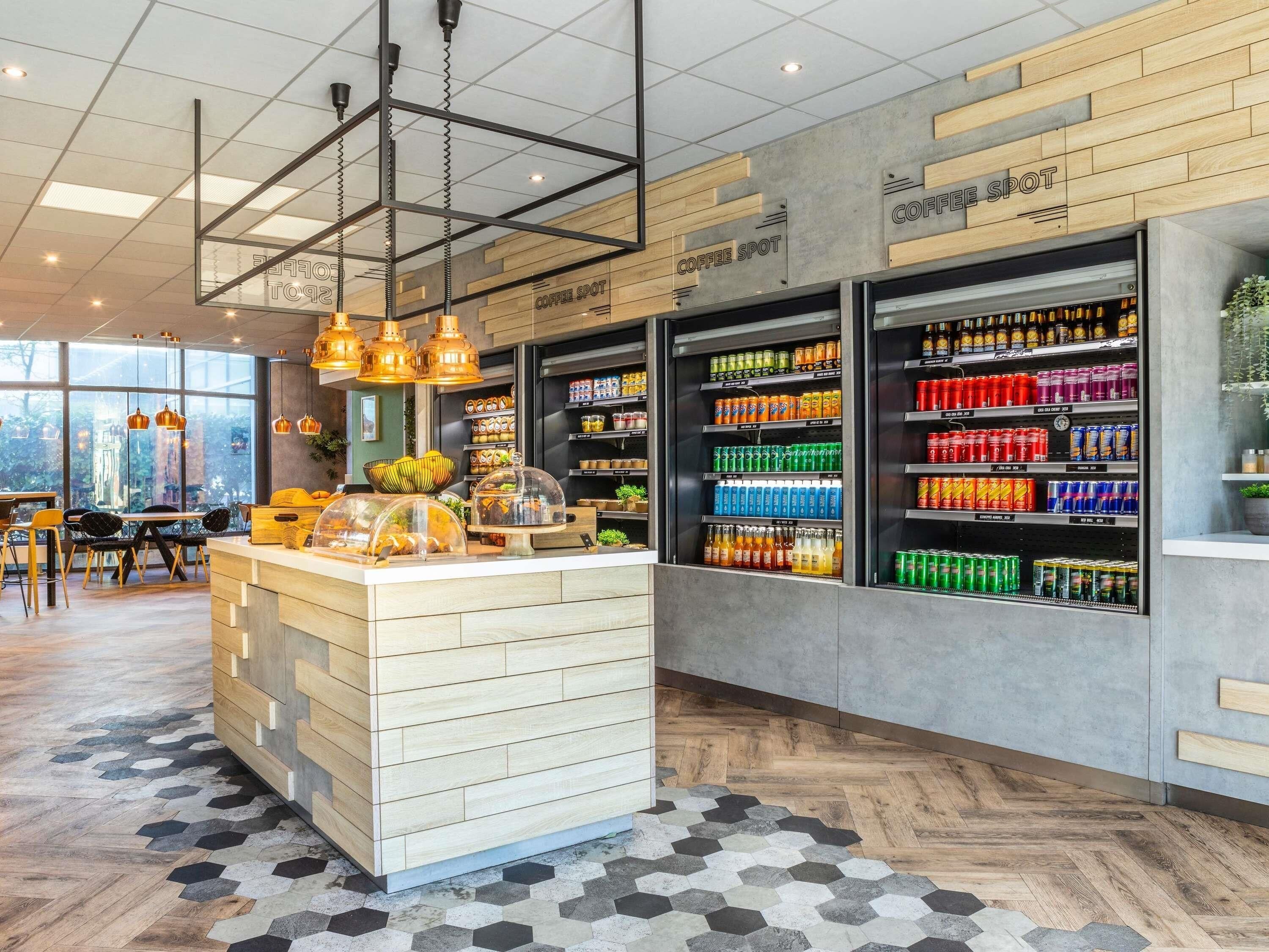 Interior moderno de una cafetería con una barra central, estantes con bebidas y un suelo con patrón de espiga.