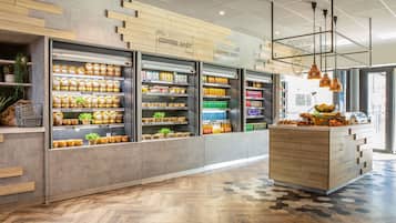 A modern coffee shop interior with wooden shelves displaying various food items and a central counter with baked goods.