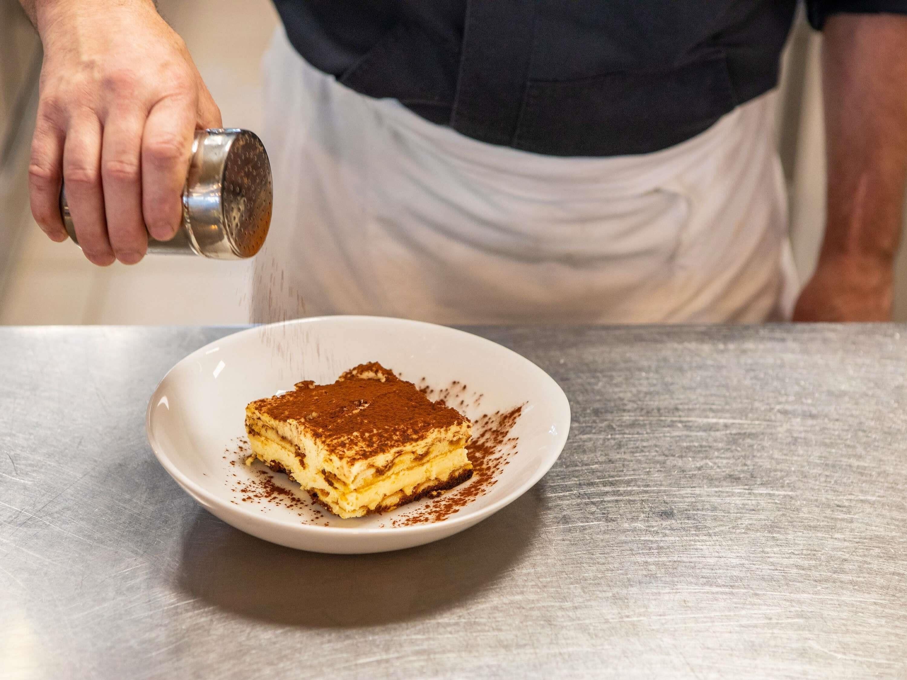 Une personne saupoudrant du cacao en poudre sur un dessert.