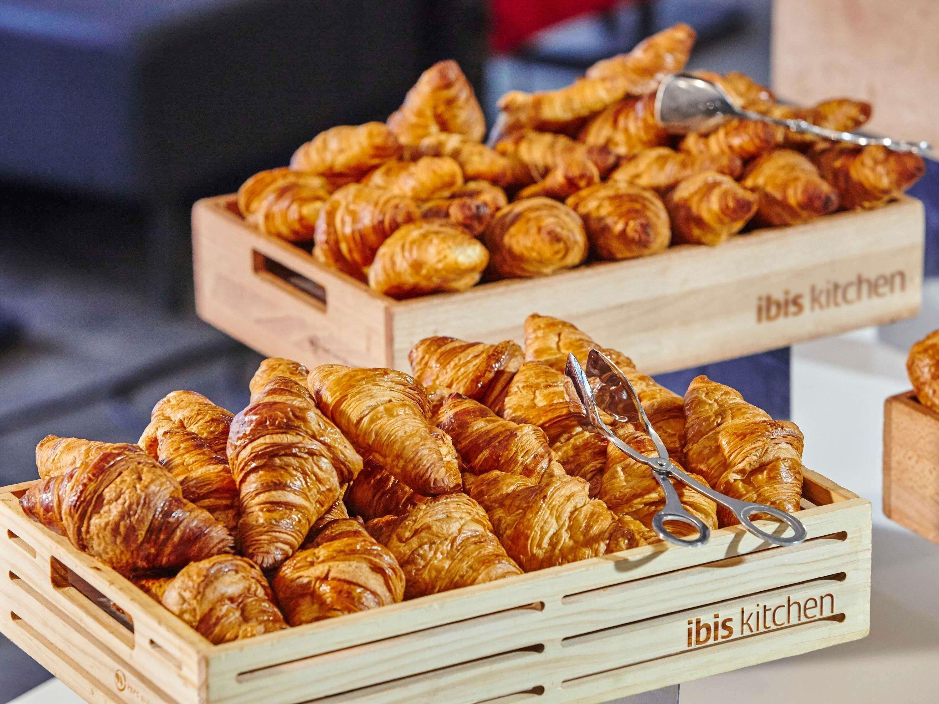 Cajas de madera llenas de cruasanes y un par de pinzas, con la etiqueta 'ibis kitchen'.