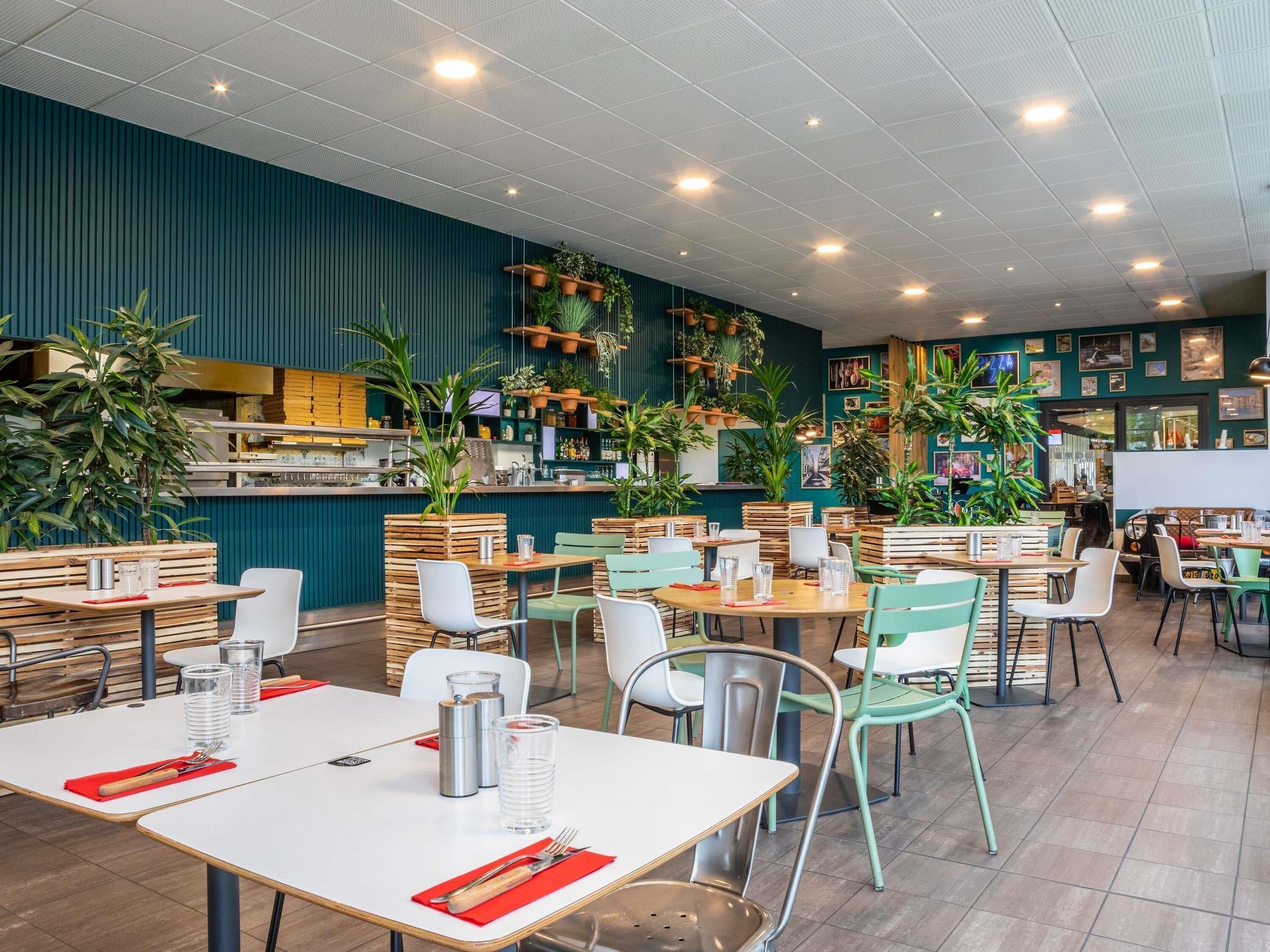 L’intérieur d’un restaurant, avec de nombreuses tables et chaises, un bar et diverses plantes en pot.