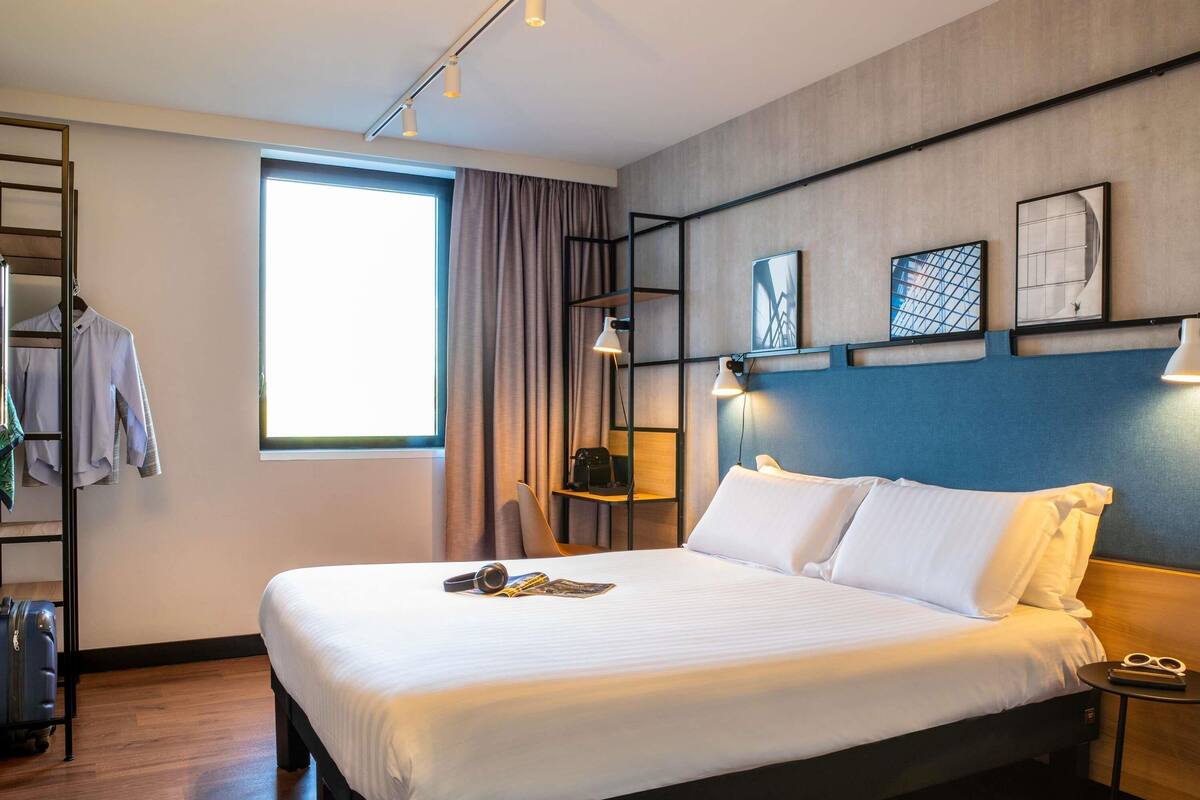 Une chambre d’hôtel moderne avec un grand lit, une armoire, un bureau et une fenêtre avec des rideaux.