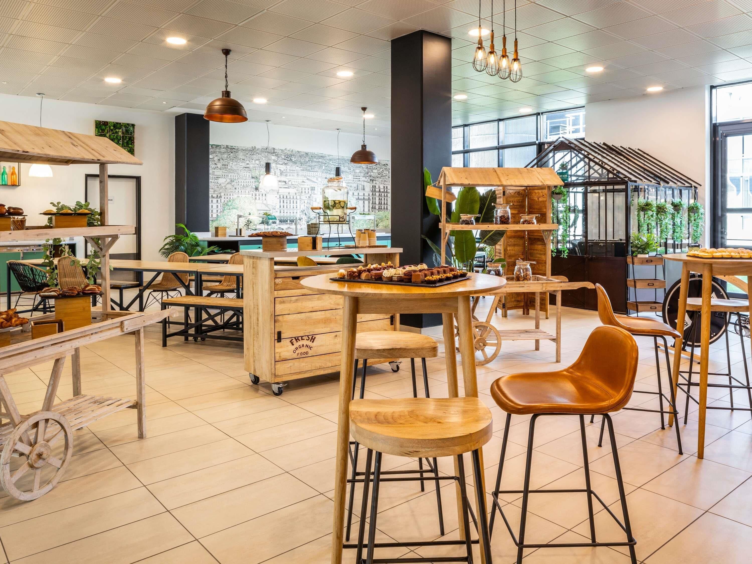 A modern cafe with wooden furniture, a cityscape view, and a variety of food displays.