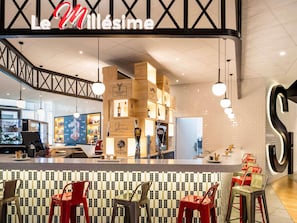 A modern bar area with a counter displaying various bottles and glasses, a seating area with red chairs, and a prominent 'Le Millésime' sign above the bar. - ibis Paris CDG Airport (Tremblay-en-France)