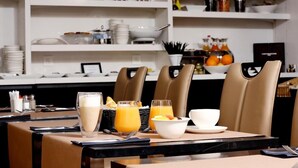 Une table mise pour le petit-déjeuner, avec une nappe pour deux personnes, comprenant un saladier de fruits, deux verres de jus d’orange et un verre de lait.