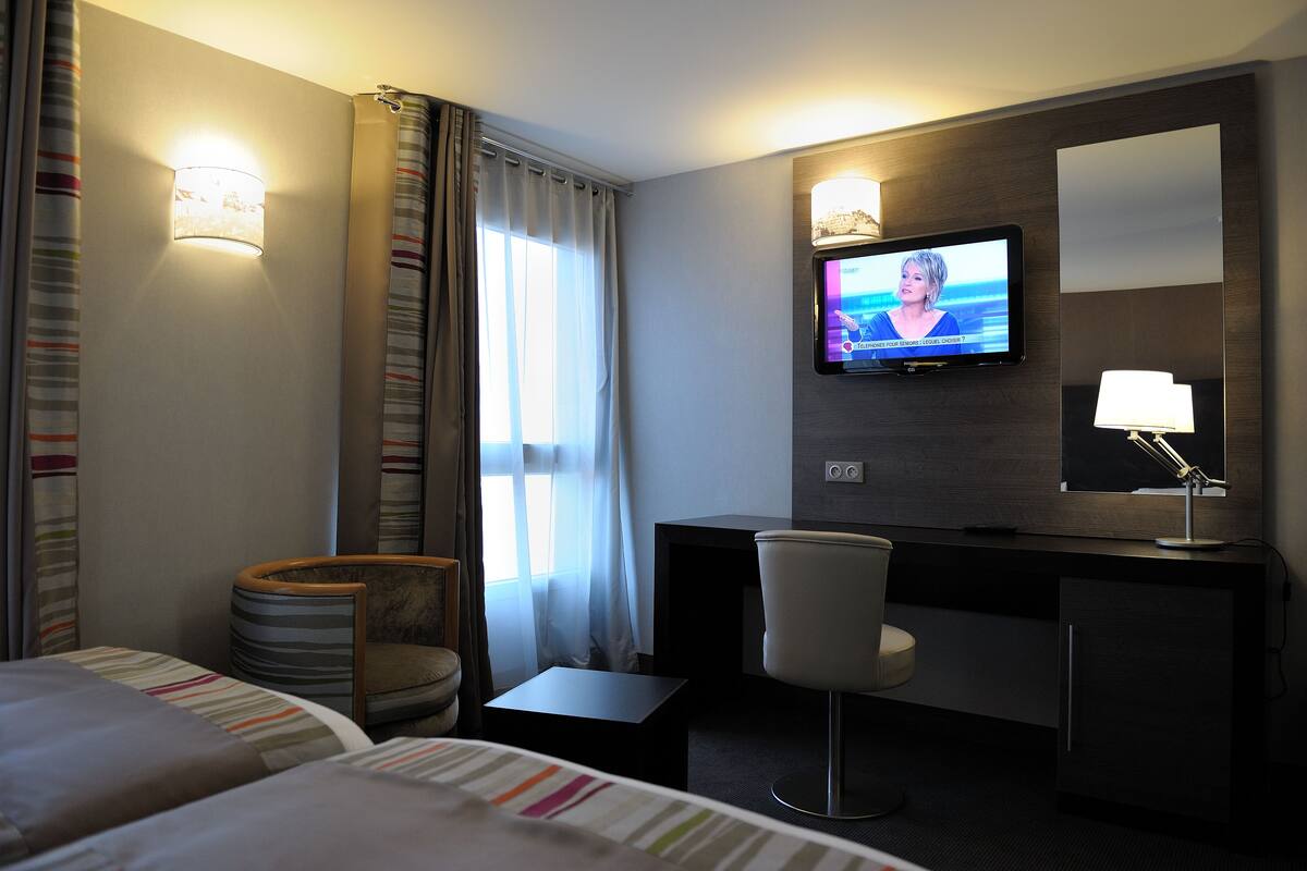 A hotel room with two beds, a desk, a chair, a television, and a lamp.