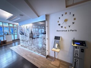 Um saguão de hotel com um relógio de parede grande, uma recepção e um quiosque digital.