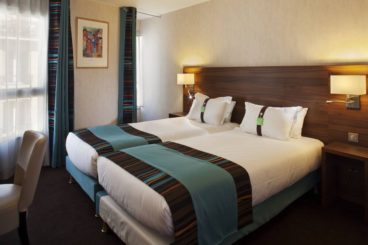 A hotel room with two beds, a desk, a chair, and a painting on the wall.