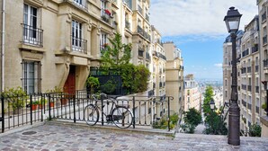 A cobblestone street with a bicycle parked on a metal railing, overlooking a cityscape with buildings and a clear sky. - Holiday Inn Paris - Montmartre by IHG (Paris)