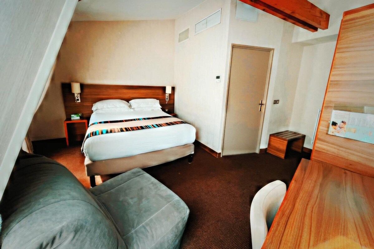 Quarto de hotel com cama, mesa de cabeceira, abajur e cabeceira de madeira.