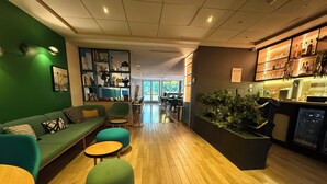 A modern interior with a green sofa, teal chairs, a wooden floor, and a bar area with plants. - Holiday Inn Paris - Montmartre by IHG (Paris)
