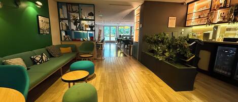 Un interior moderno con un sofá verde, sillas turquesa, suelo de madera y una zona de bar con plantas.