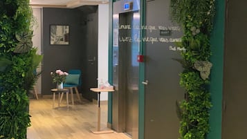 Zona de recepción con pared verde, mostrador, una silla y una puerta con un letrero.