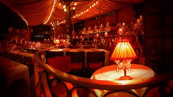 A dimly lit restaurant with round tables, red chairs, and string lights.