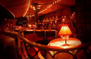 A dimly lit restaurant with round tables, red chairs, and string lights. - Holiday Inn Paris - Montmartre by IHG (Paris)