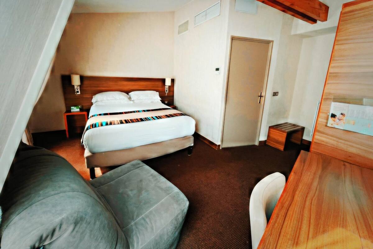A hotel room with a bed, bedside table, lamp, and a wooden headboard.