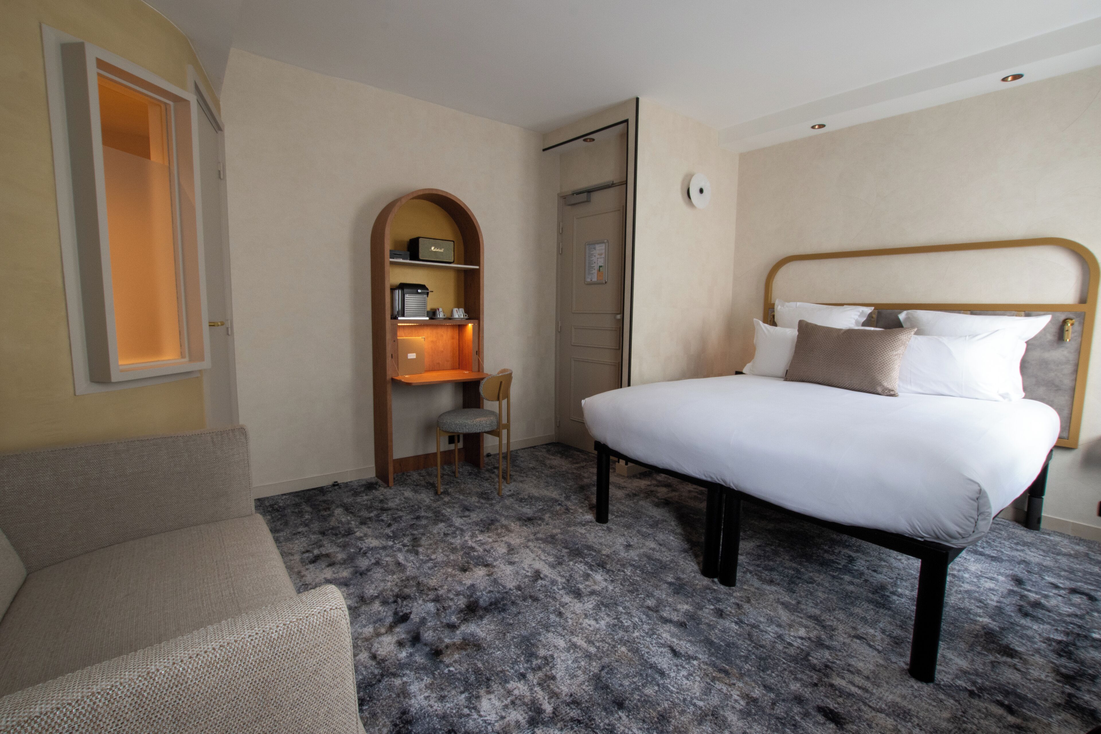 A hotel room with a bed, a chair, a desk with a chair, and a wardrobe.