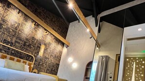 Un dormitorio moderno con una cama, un sillón amarillo, una mesita y un adornado en la pared.