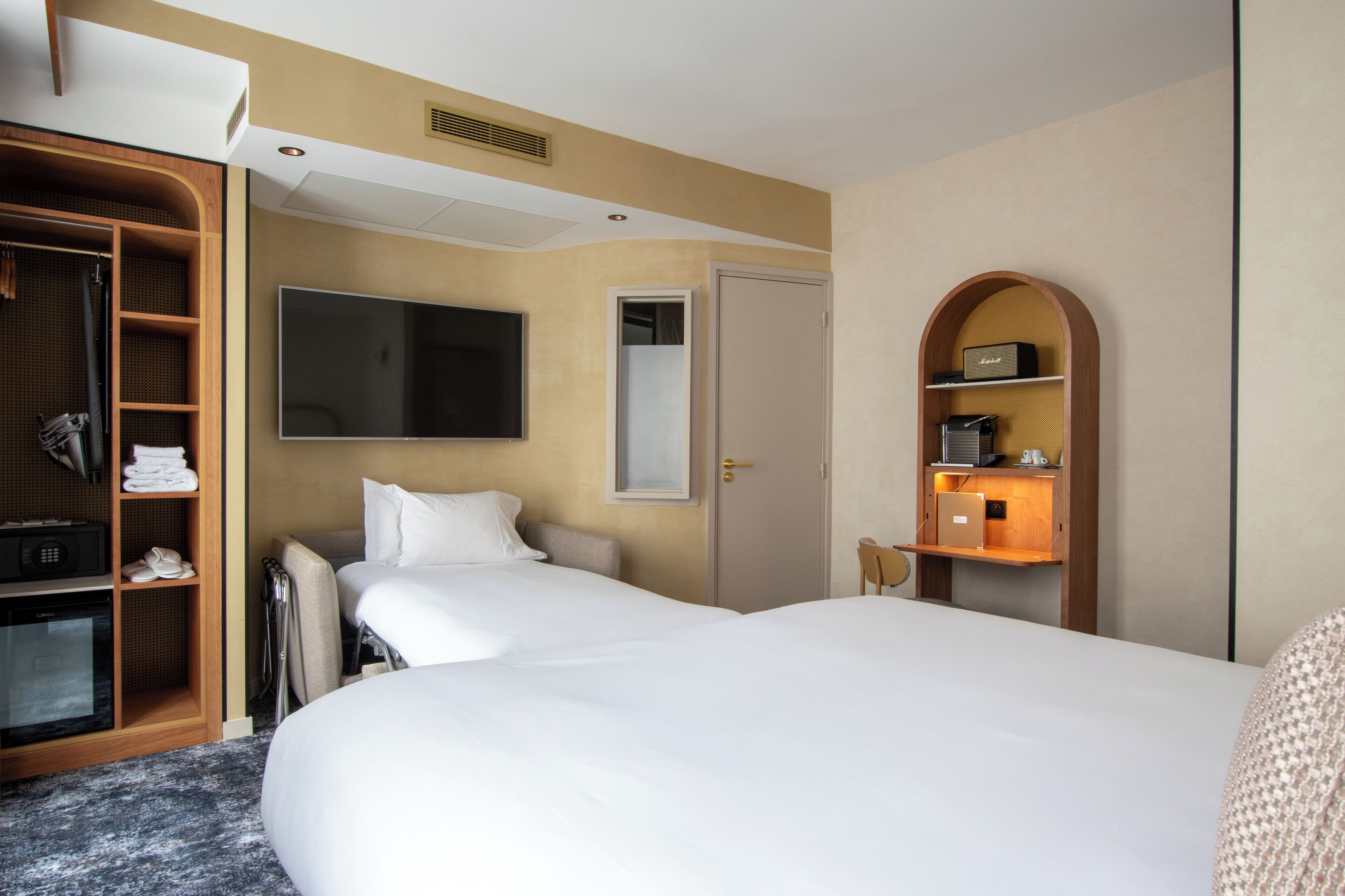 Une chambre d’hôtel avec deux lits, une télévision, une armoire et un petit bureau avec une lampe.
