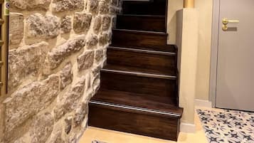 A staircase with stone walls, wooden steps, and a patterned floor.