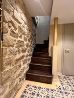 A staircase with stone walls, wooden steps, and a patterned floor.